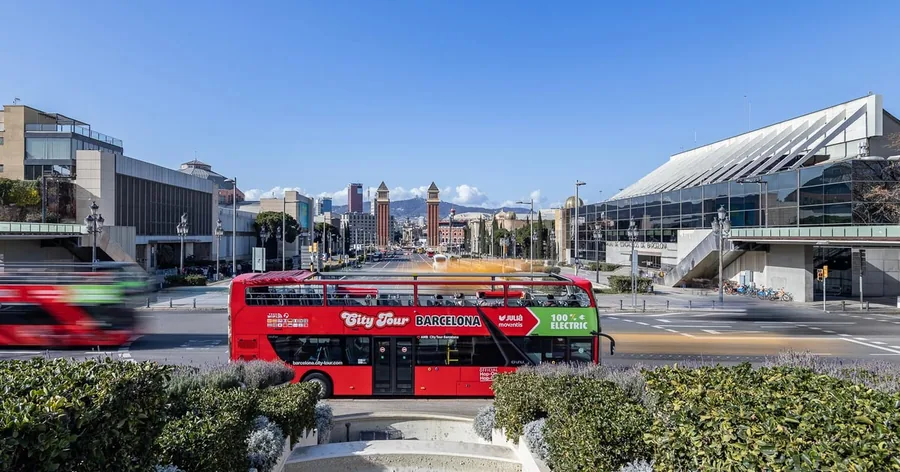 Ein roter Sightseeing-Bus an der Plaça d'Espanya, dahinter die alten Ausstellungshallen