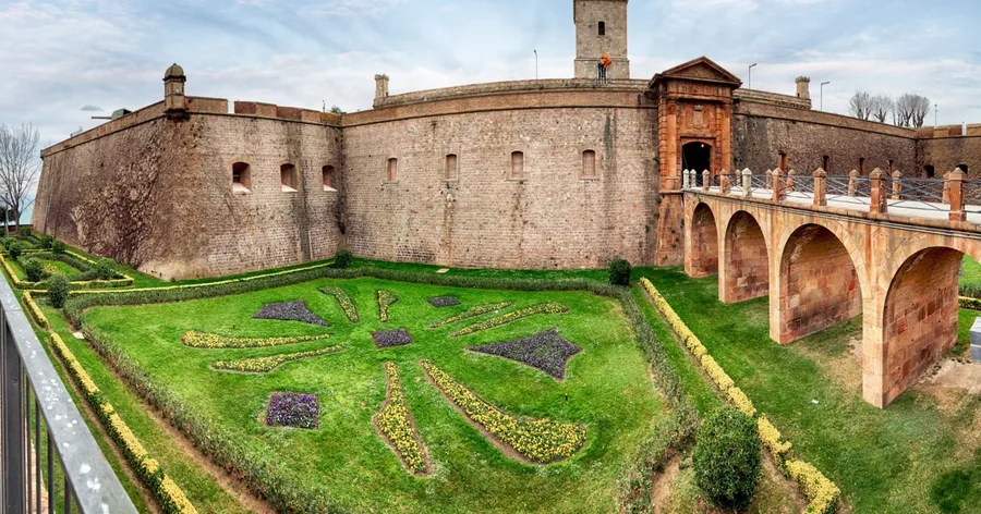 Das Kastell von Montjuïc von oben: dicke Steinmauern, ein Blumenbeet-Emblem im Burggraben und die gewölbte Eingangsbrücke