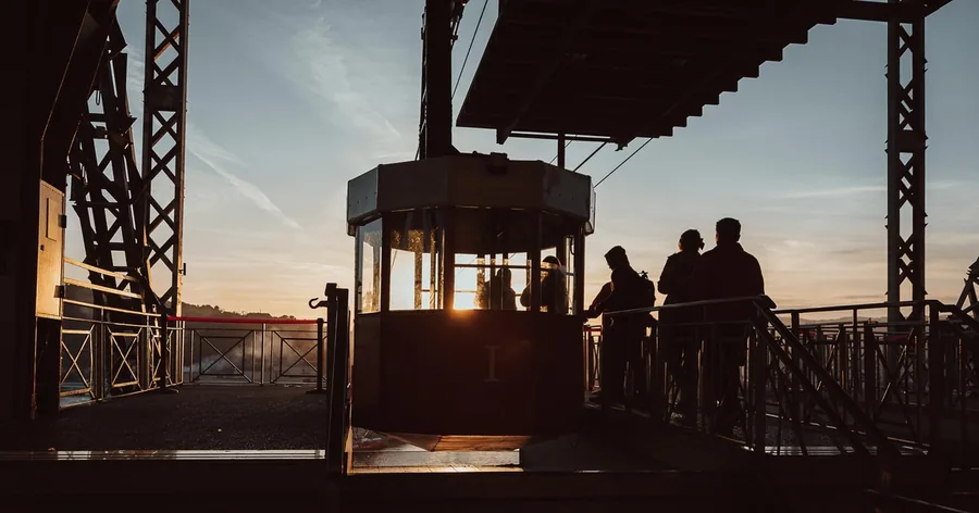 Menschen als Silhouetten warten bei Sonnenuntergang neben einer Seilbahnkabine an einer Bergstation