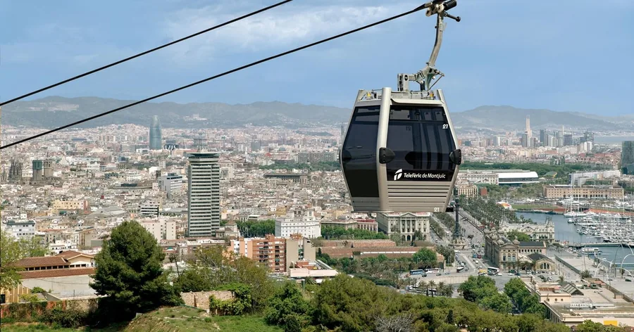 Eine Gondel der Seilbahn von Montjuïc schwebt über der Stadt, rechts der Hafen mit seinen Kränen